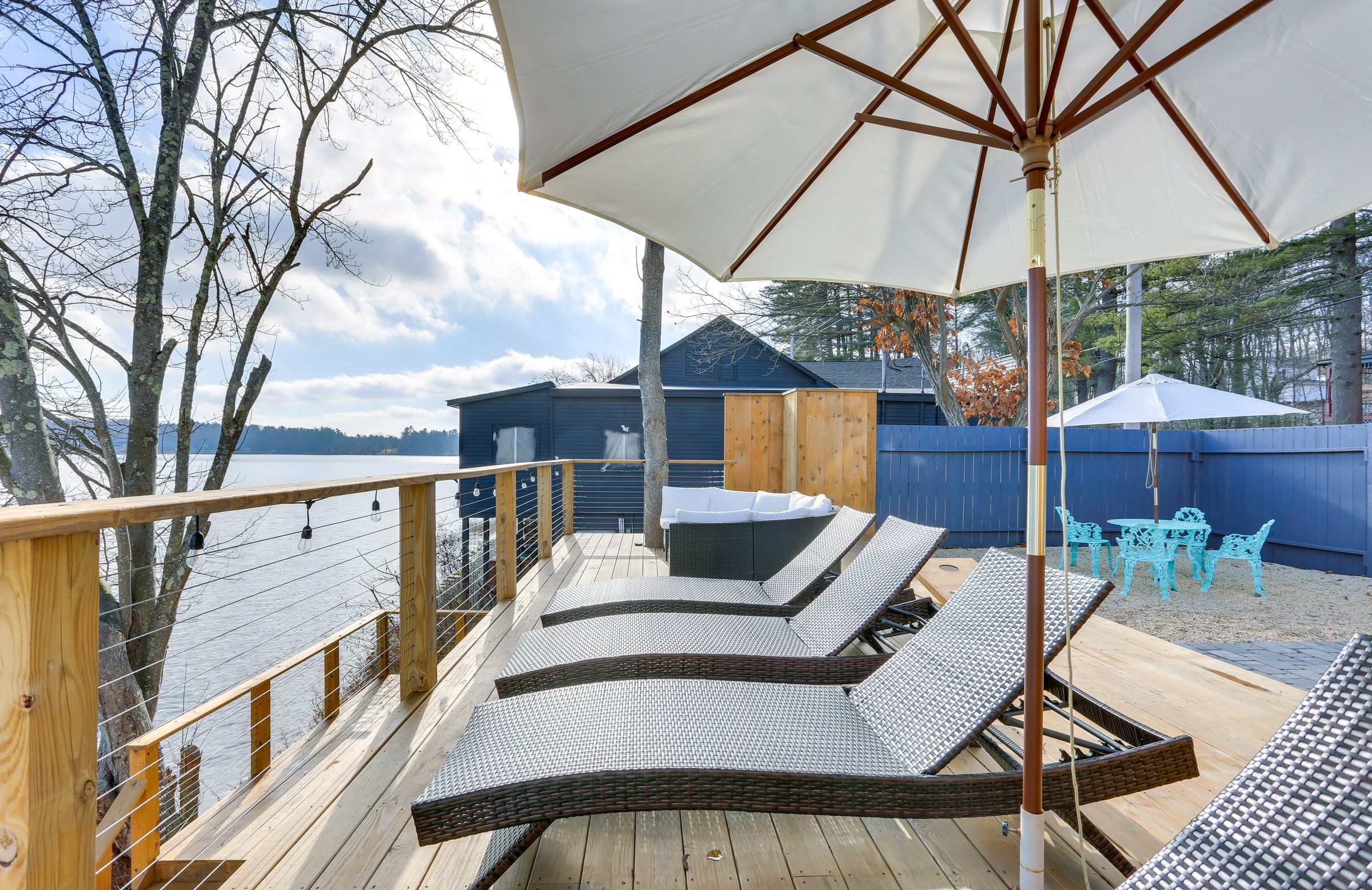 Woven loungers lined up under a market umbrella on the lakefront deck, water on both sides.