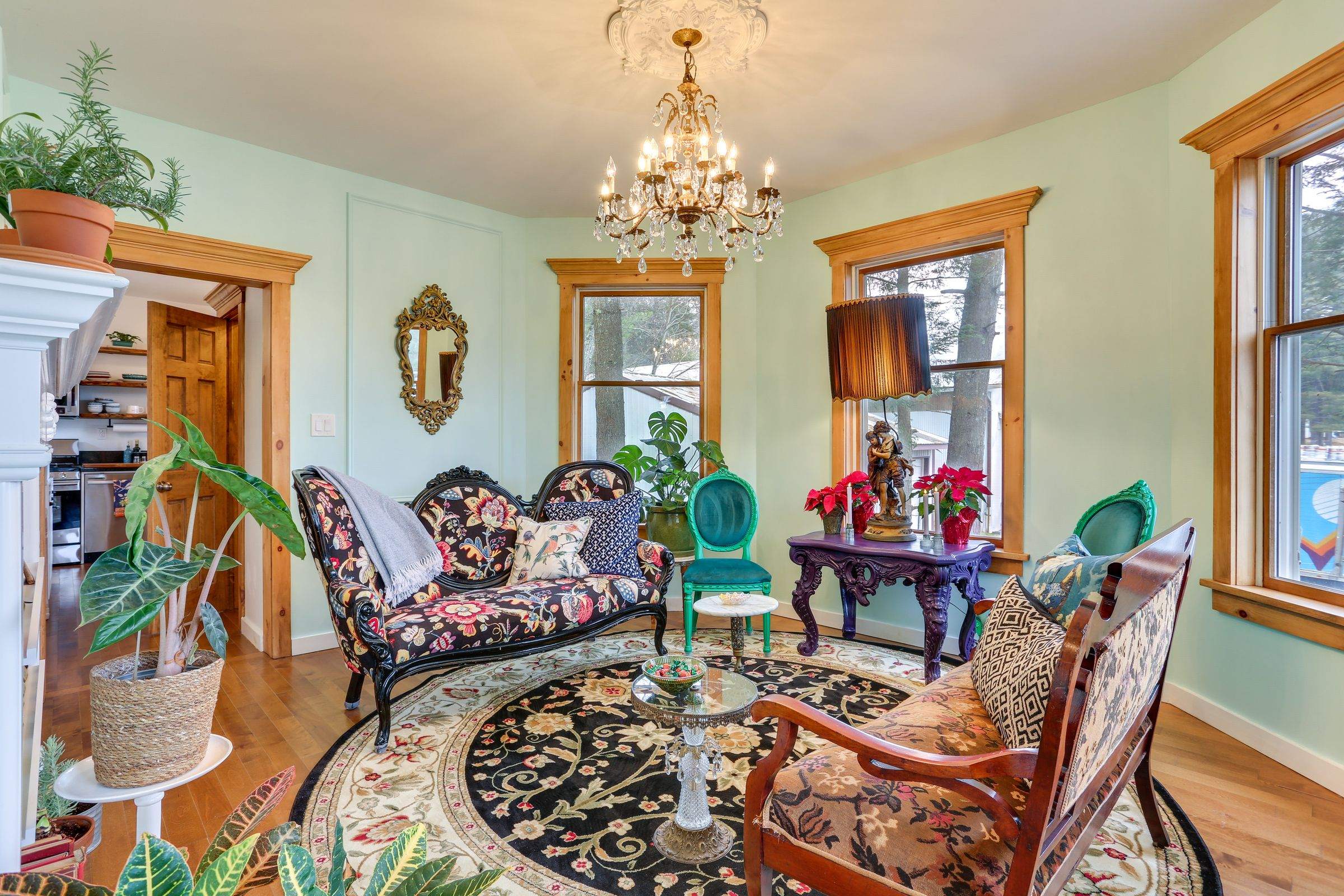 The green parlor with a crystal chandelier, antique floral settee, patterned rug and tall windows.