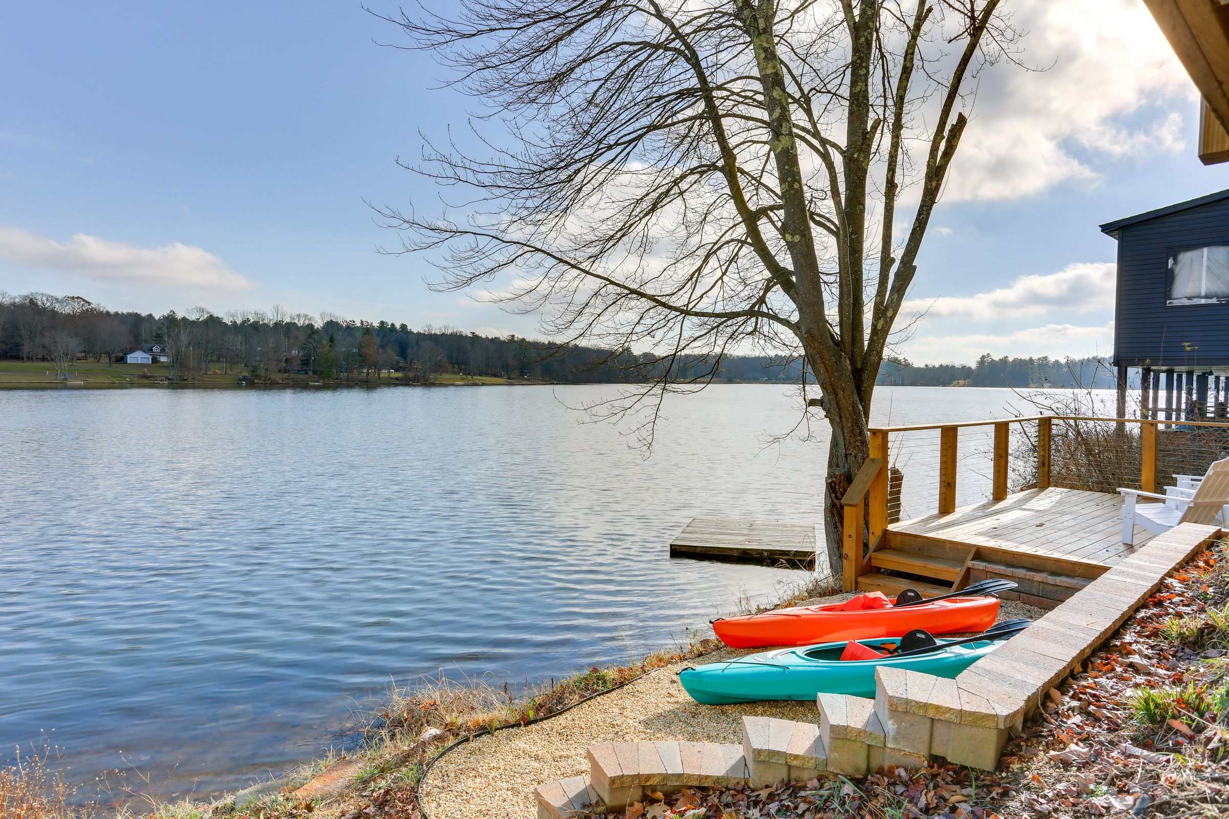 Two kayaks pulled up on the private shoreline beside the deck, open lake stretching to the far bank.